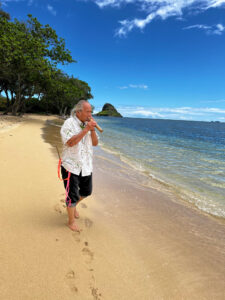 Uncle Calvin Hoe walks along a beach in Hawaii while playing the bamboo nose flute.