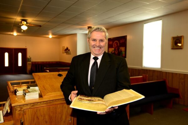 A man stands in in a church with a large hymnbook in his hands