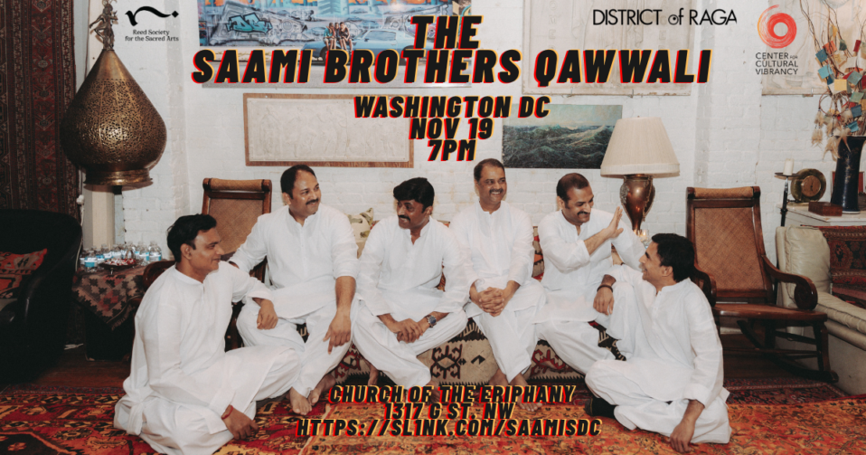 6 men in white clothes sit on the floor on a multi-colored rug