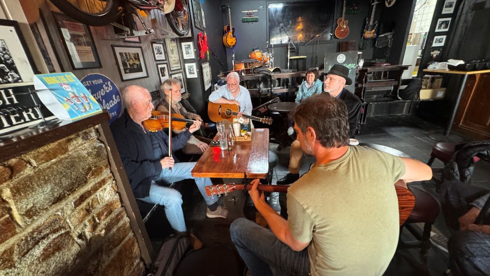 A group of musicians sit around a table in a pub and play music.