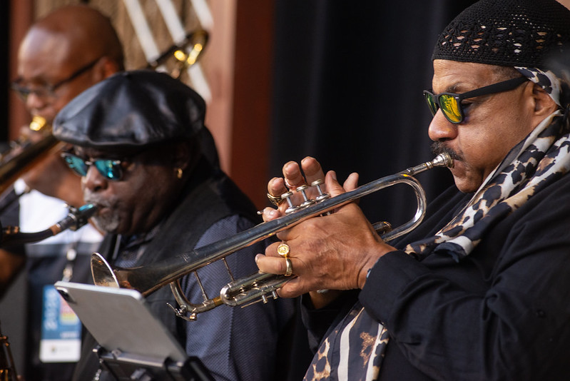 Three men wearing all black blow into horns.