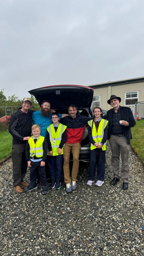 4 adults stand with three children in front of a car.